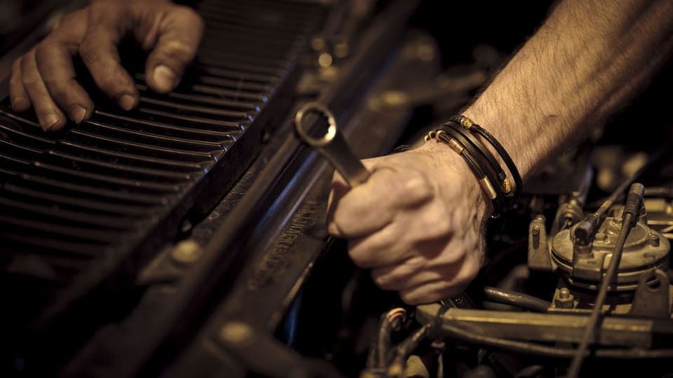 Hands using a wrench on a car engine. Stock photo.